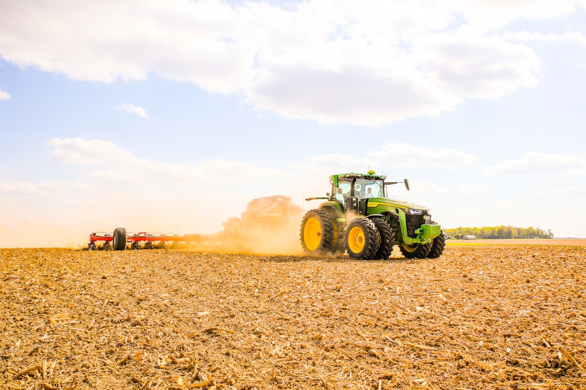 Traktor mit Sävorsatz bei der Aussaat auf einem Feld, Staubschleier hinter dem Gerät